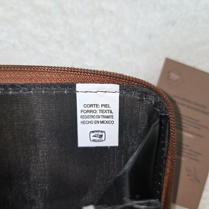 Close-up of a black fabric pouch with a brown zipper and a label on a textured white background.