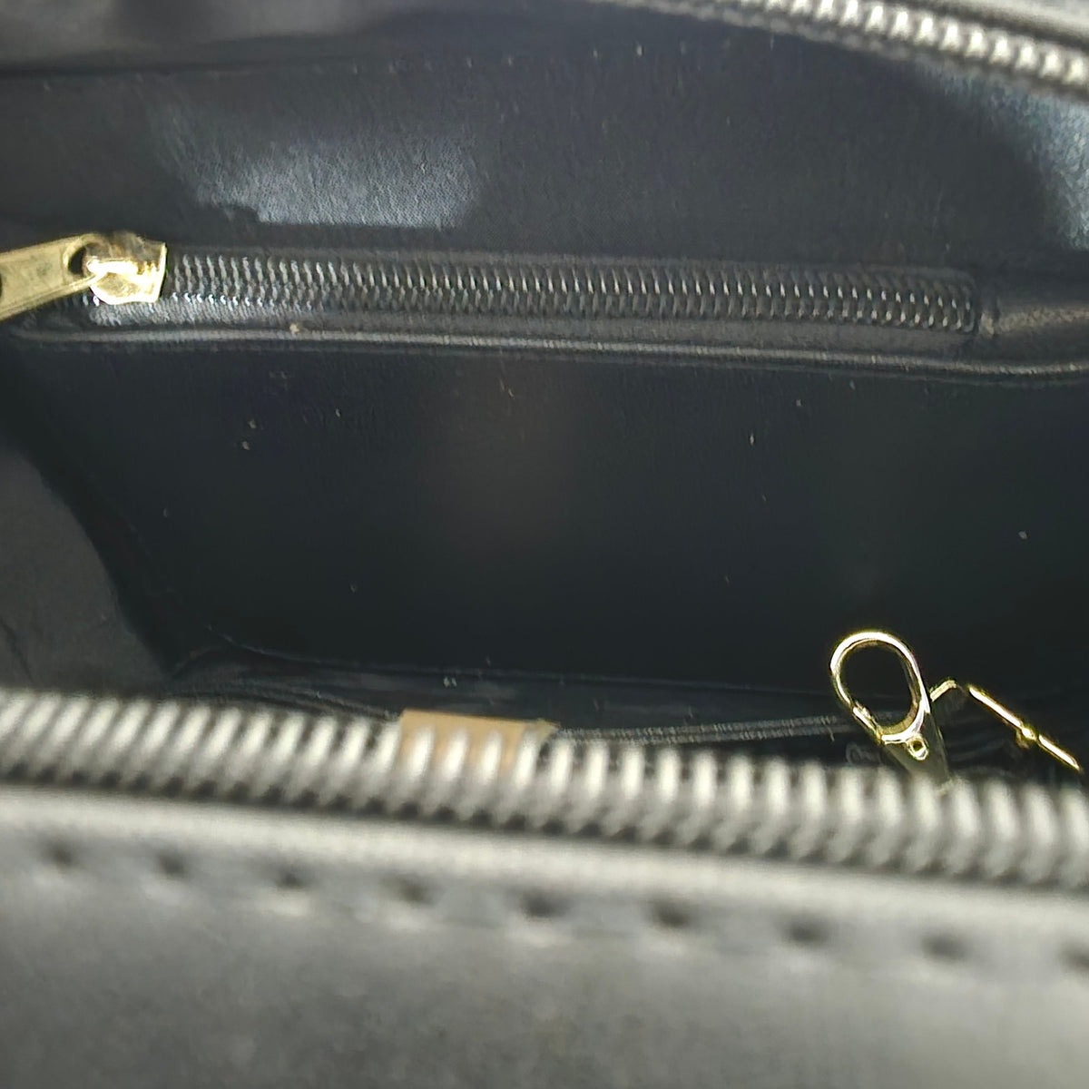 Close-up of a black handbag with gold zippers